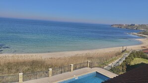 Une vue sur la côte, avec une plage de sable fin, une piscine et une côte rocheuse qui s’étend au loin.
