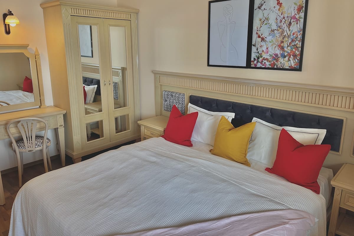 Een slaapkamer met een groot bed, een kledingkast, een bureau en twee kunstwerken in lijsten aan de muur.