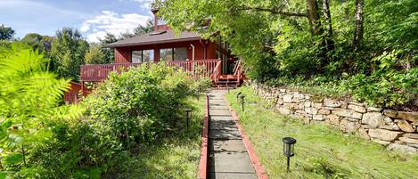 A red wooden house with a stone wall and a pathway leading to it.