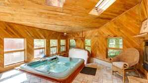 A wooden cabin with a hot tub, wicker furniture, and large windows.