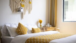 A neatly made bed with white and yellow bedding, a macrame wall hanging, and a small table with a vase of flowers. - Private running bar post Dali ancient shop (Dali City)