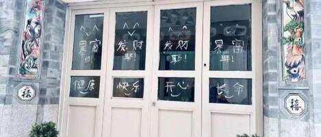 Fachada de edificio con una puerta de entrada amplia, paneles decorativos en la pared y un cartel sobre la puerta.