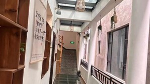 A narrow hallway with a staircase leading to an upper floor. The walls are adorned with wooden shelves and hanging plants. - Private running bar post Dali ancient shop (Dali City)