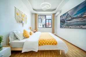 A bedroom with a bed, a window, a painting, and a macrame wall hanging.