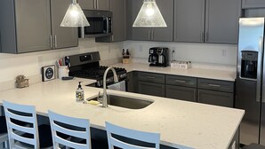 A modern kitchen with grey cabinets, a central island with bar stools, stainless steel appliances, and pendant lighting. - Beautiful Family Beach Retreat-Pool, Marina, and minutes to the beach. (Lewes)