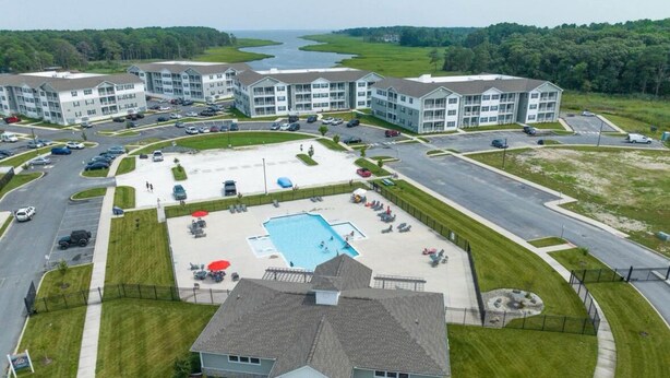 An aerial view of a residential complex with multiple apartment buildings, a central swimming pool, and a parking area. - Beautiful Family Beach Retreat-Pool, Marina, and minutes to the beach. (Lewes)