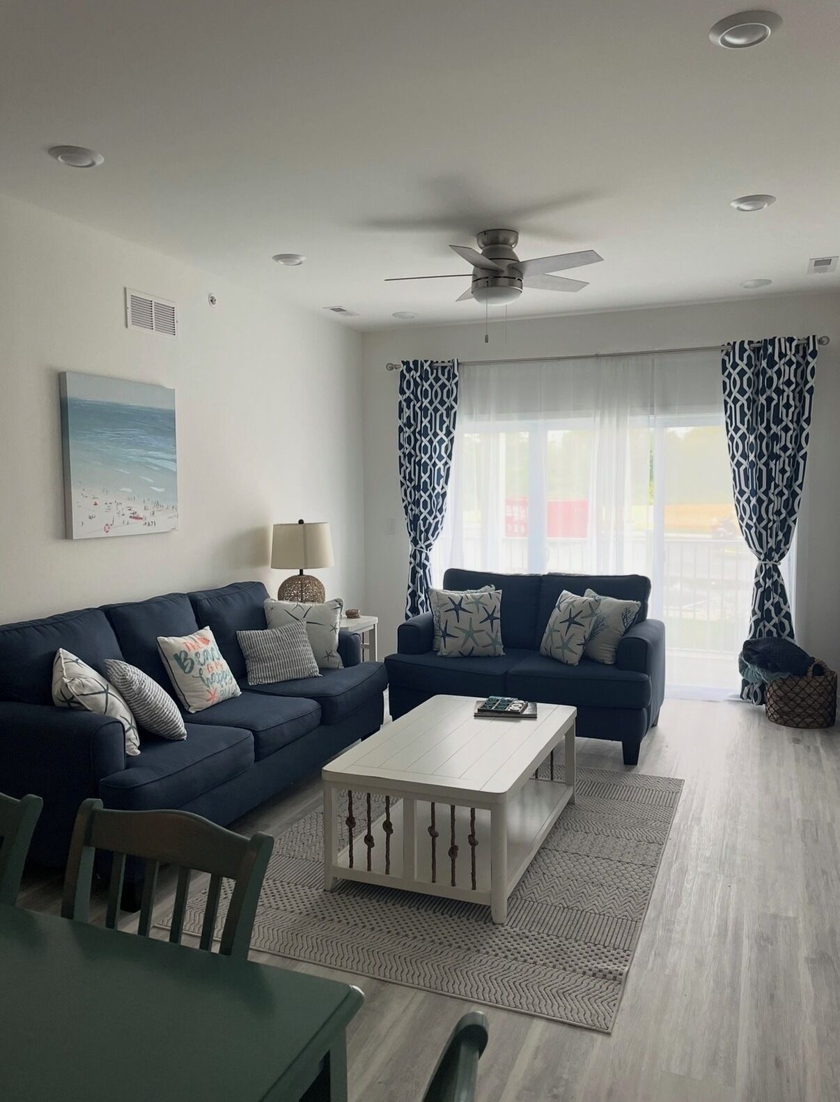 A living room with two sofas, a coffee table, a ceiling fan, and a window with patterned curtains.