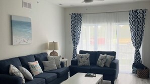 A living room with two sofas, a coffee table, a ceiling fan, and a window with patterned curtains. - Beautiful Family Beach Retreat-Pool, Marina, and minutes to the beach. (Lewes)