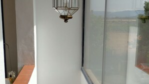 Een smalle trap die uitkomt op een plateau met een groot raam, een hanglamp en een houten vloer.