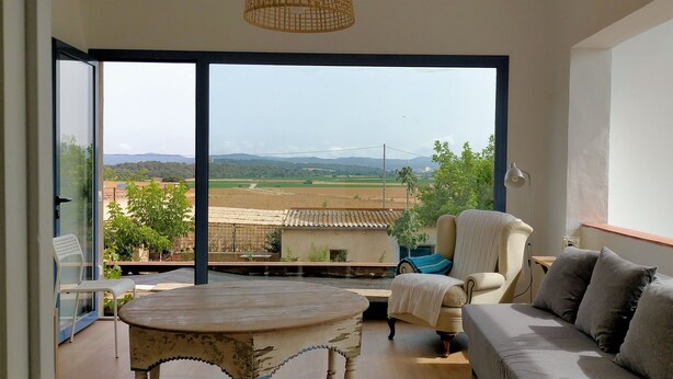 Een balkon met uitzicht op een landelijk landschap, een bank, een stoel en een kleine tafel.