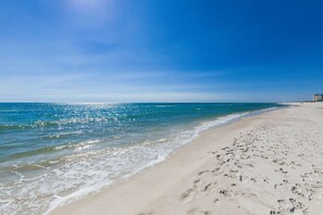 Ein Strand mit klarem, blauem Wasser, sandigem Ufer und Fußabdrücken im Sand.