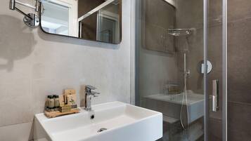 A modern bathroom with a white sink, a mirror, and a glass-enclosed shower.