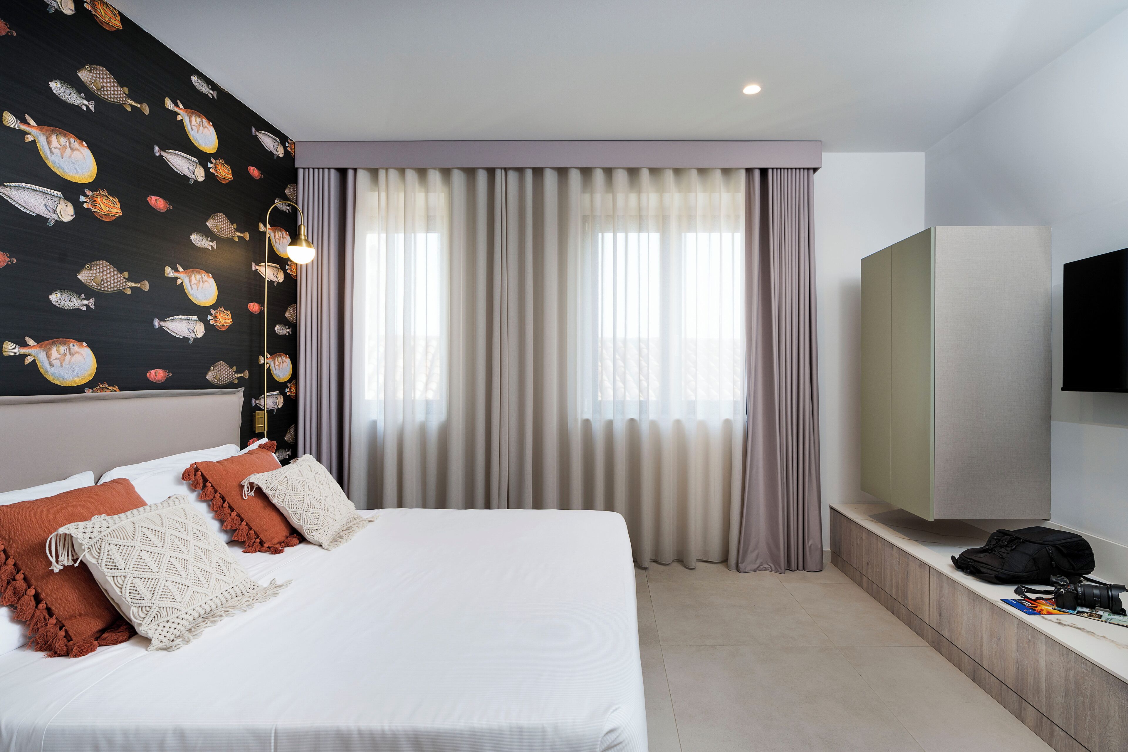 Una habitación de hotel con cama, televisor, armario y cortinas.