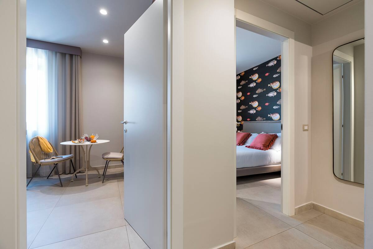 Quarto de hotel moderno com uma cama, uma pequena mesa com cadeiras e um espelho grande.