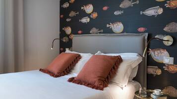 A neatly made bed with white linens and two brown pillows, a bedside table with a glass of water and a book, and a wall with a fish pattern.
