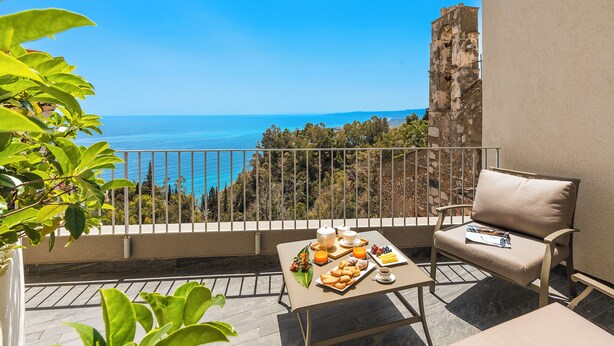 A balcony with a table set for breakfast, a chair, and a view of the sea. - Belduomo (Taormina)