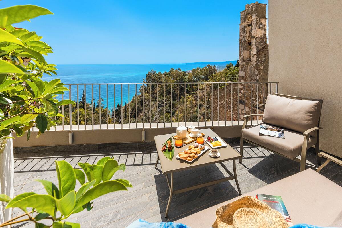 Varanda com mesa posta para o café da manhã, uma cadeira e vista para o mar.