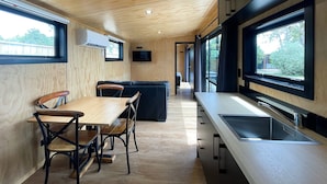 A modern kitchen with a wooden ceiling, a dining area with a table and chairs, and a large window providing a view of the outdoors. - Havelock North Holiday Park  (Havelock North)