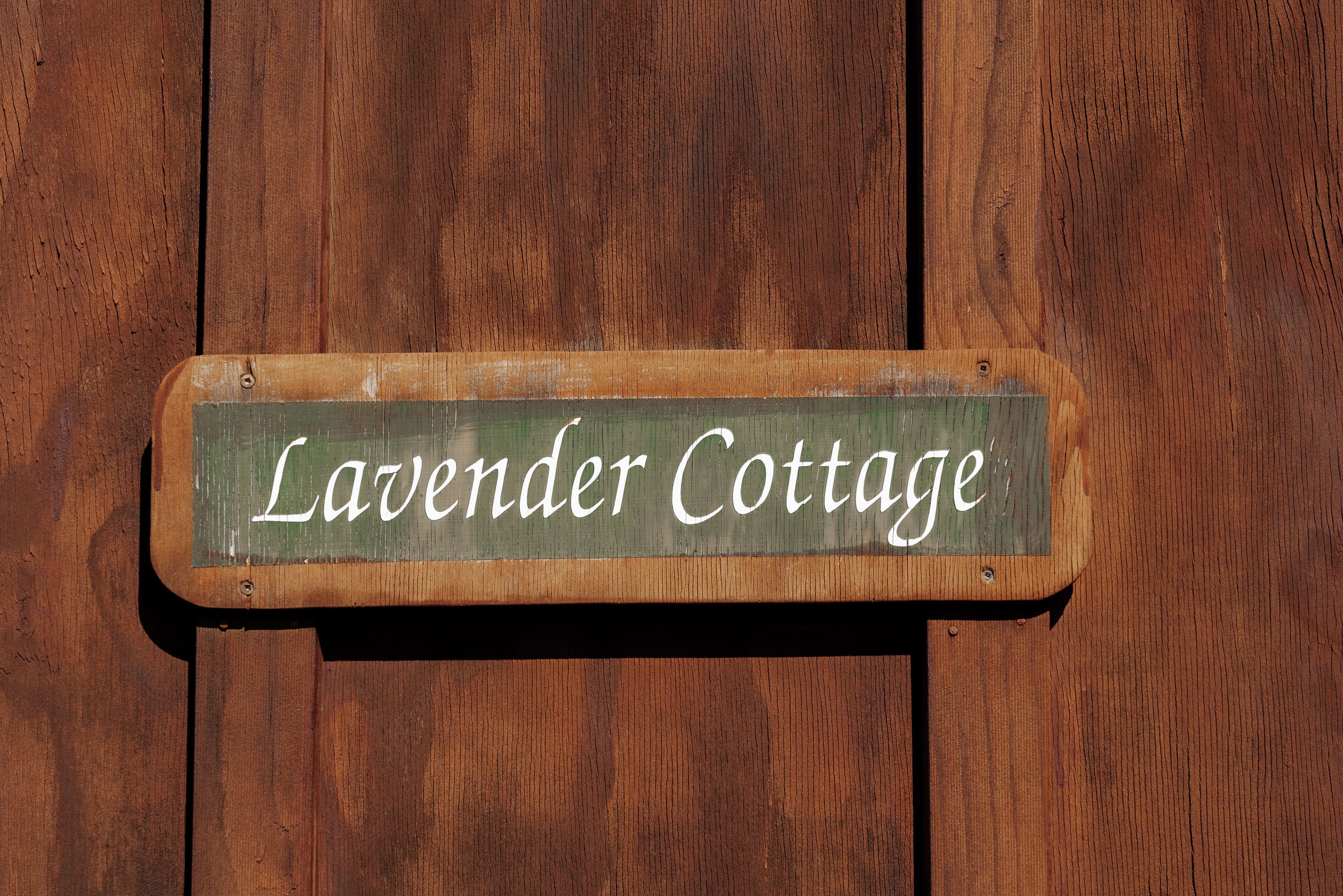 Een houten bord met de tekst 'Lavender Cottage' op een houten achtergrond.
