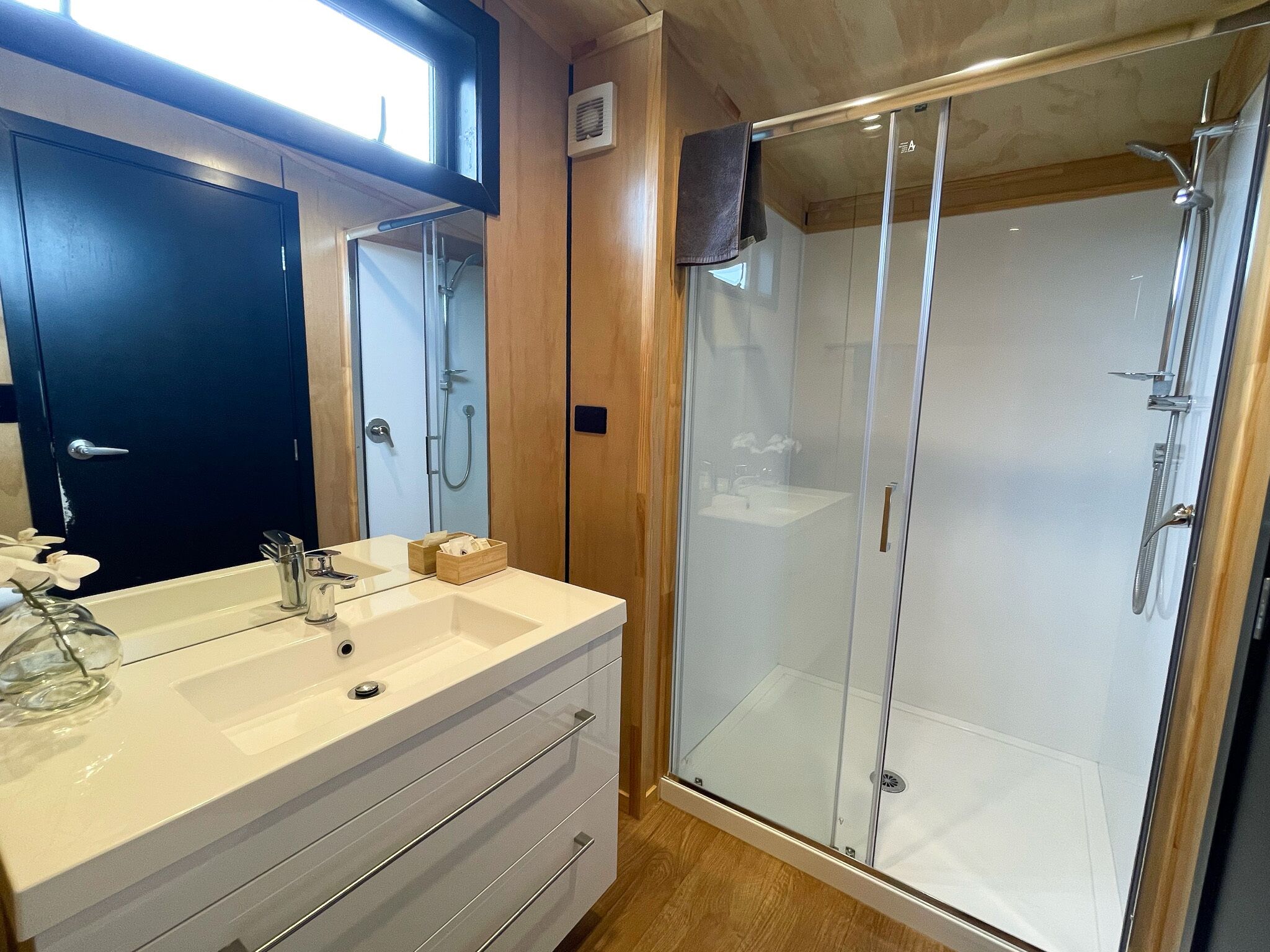 A modern bathroom with a glass-enclosed shower, a double sink vanity, and wooden paneling.