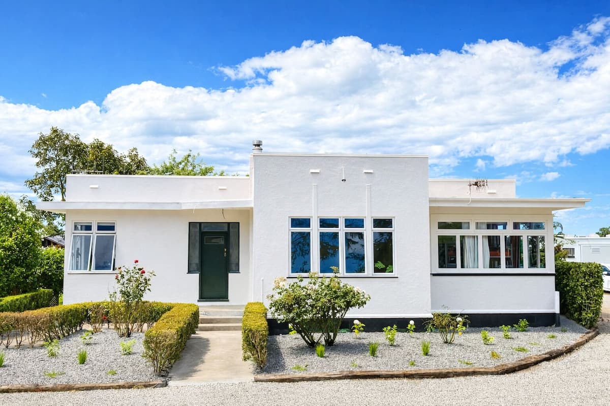 Een modern huis met twee verdiepingen, een witte gevel, een groene deur en een grindpad.