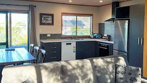 A modern kitchen with a dining area, a sofa, and a window with blinds. - Havelock North Holiday Park  (Havelock North)
