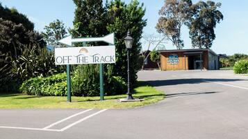 A sign for 'OFF THE TRACK' holiday park with a directional arrow, a lamp post, and a building with a reception area.