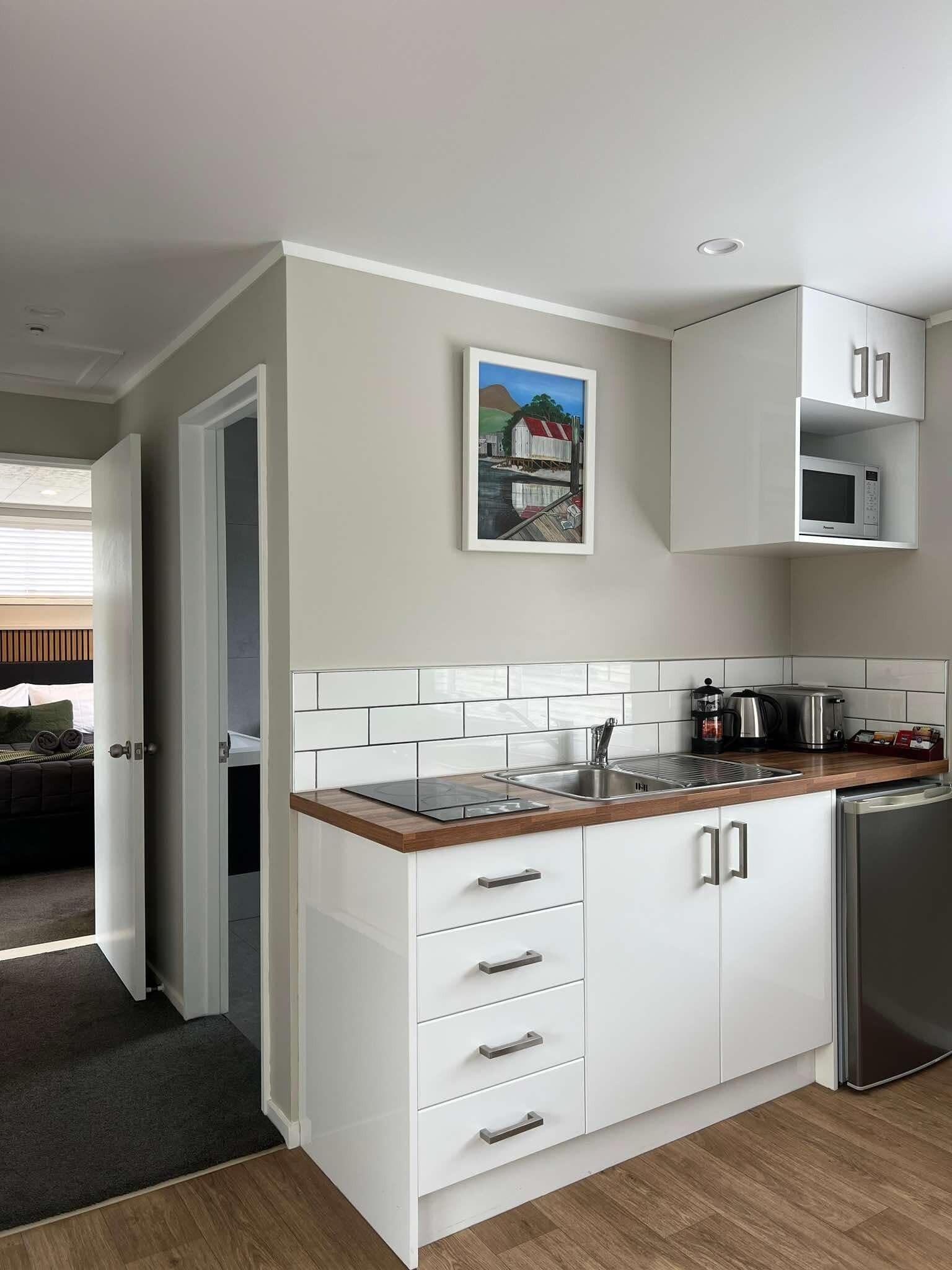 A modern kitchen with white cabinets, a wooden countertop, and a stainless steel refrigerator.