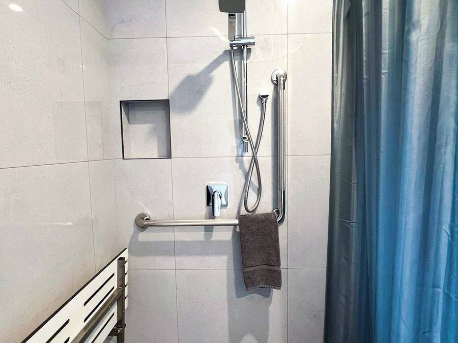 A modern bathroom with a shower, grab bar, and towel rack.