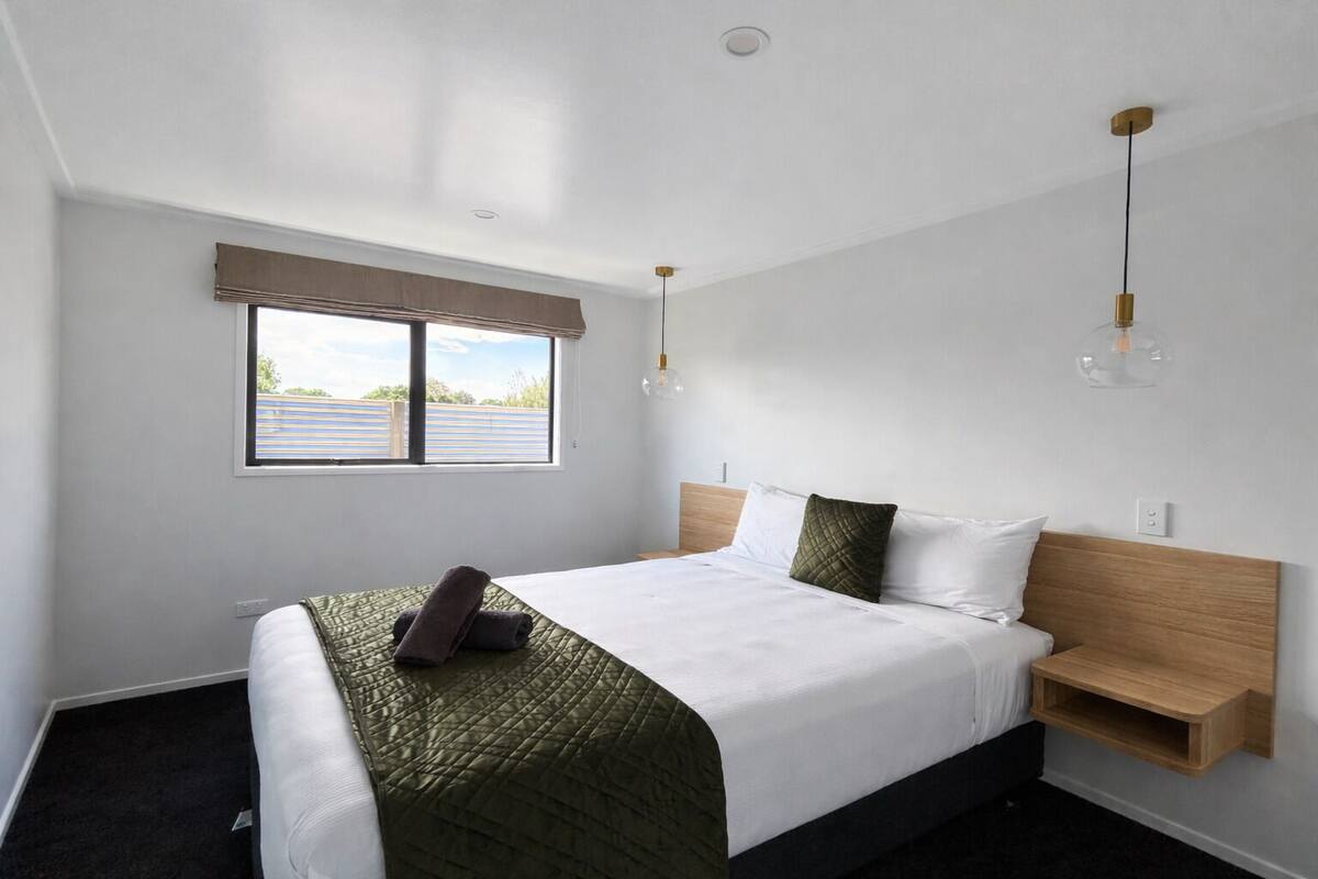 Een moderne hotelkamer met een groot bed, een houten hoofdeinde, een nachtkastje en een raam met uitzicht.