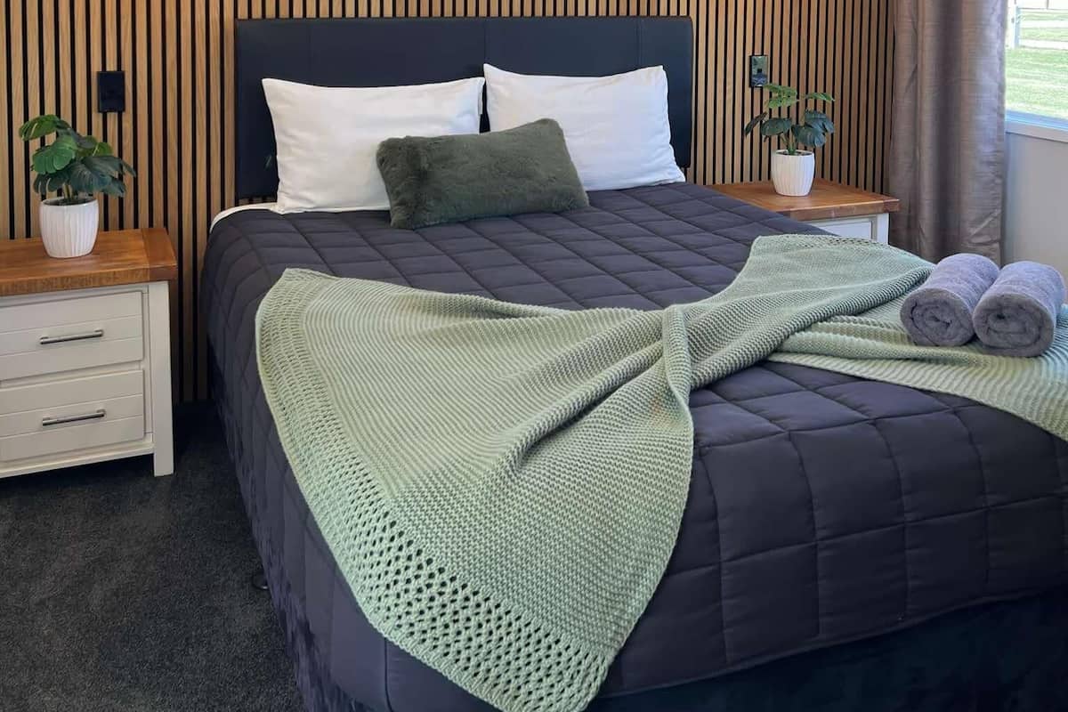 Een keurig opgemaakt slaapkamer met een bed, twee nachtkastjes, een raam met zonwering en een plafondlamp.