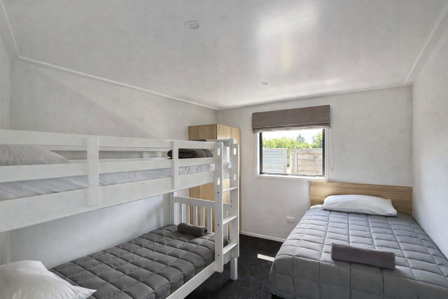 A compact room with bunk beds and a single bed, a window with a view, and a small cabinet.