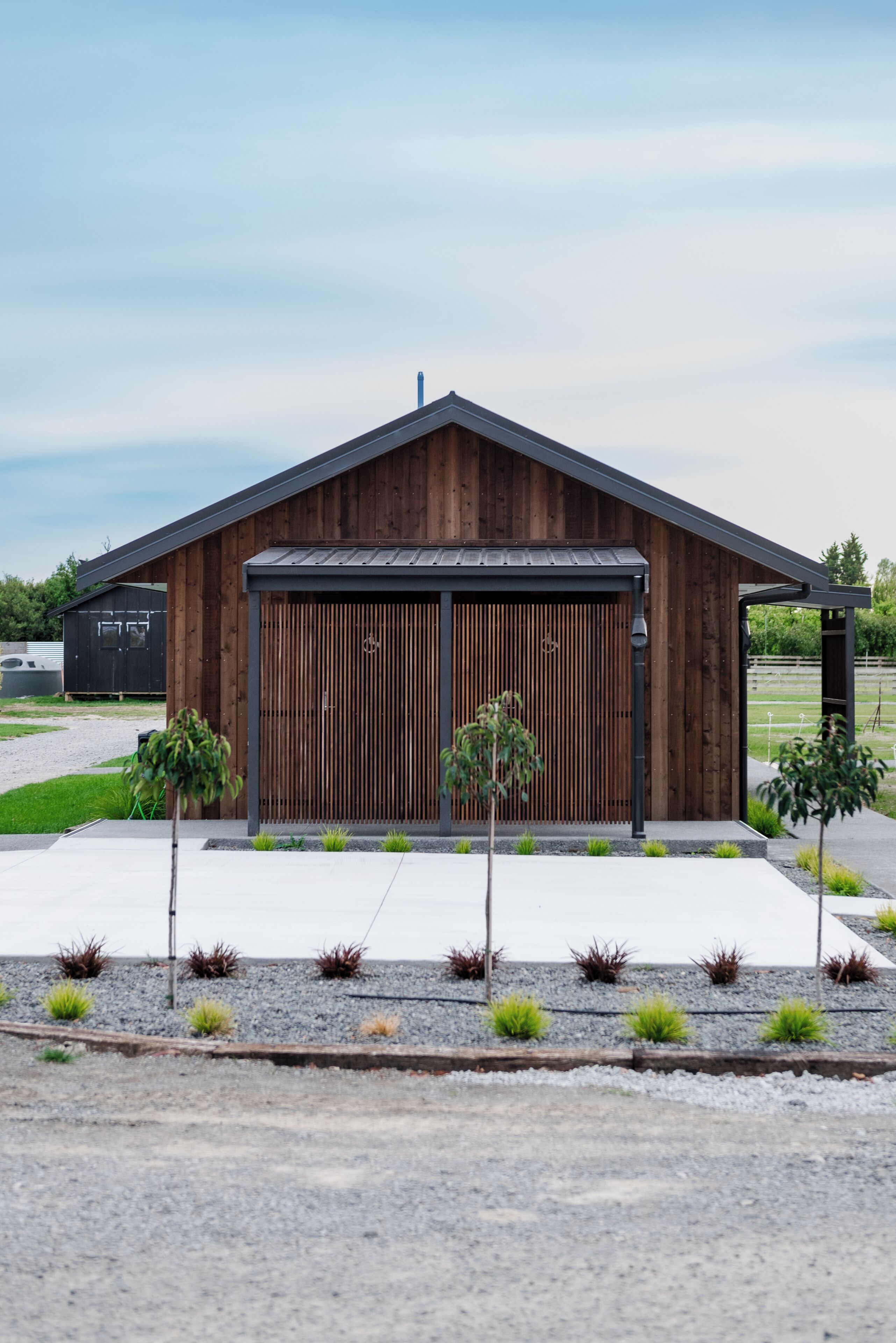 Ein modernes Gebäude mit Holzfassade, großen Garagentüren und einem Schotterweg mit kleinen Pflanzen.