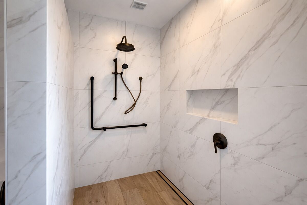 A modern shower with a handheld showerhead, a wall-mounted control panel, and a wooden floor.