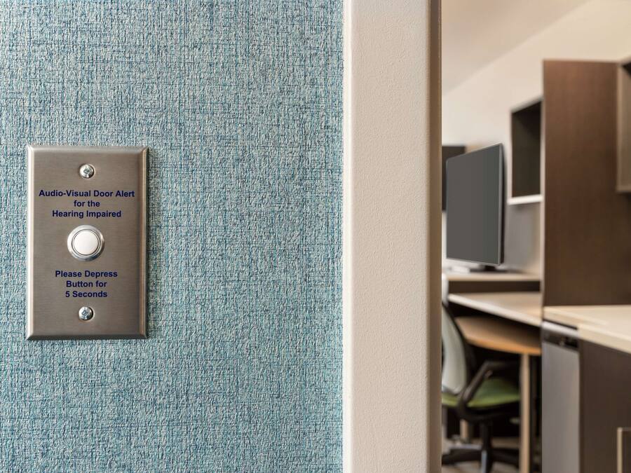 Eine Tür mit einem Audio-visuellen Alarmsystem für hörgeschädigte Personen, ein Knopf, der fünf Sekunden lang gedrückt werden muss, und Blick in einen modernen Küchenbereich.