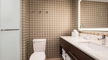 Une salle de bain avec un mur à motifs, des toilettes blanches, un lavabo avec un miroir et un porte-serviettes.