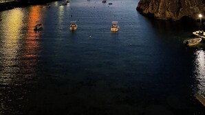 Un paysage côtier avec des bateaux ancrés dans des eaux calmes, une côte rocheuse et des bâtiments sur la gauche.