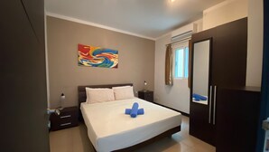Une chambre d’hôtel avec un lit, une table de chevet, une lampe, un tableau au mur et une fenêtre avec des rideaux.