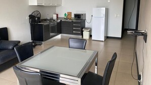 Une cuisine moderne équipée d’une cuisinière à gaz, d’un four à micro-ondes et d’un réfrigérateur. On y trouve une table à manger avec des chaises, ainsi qu’un canapé noir dans l’espace salon.