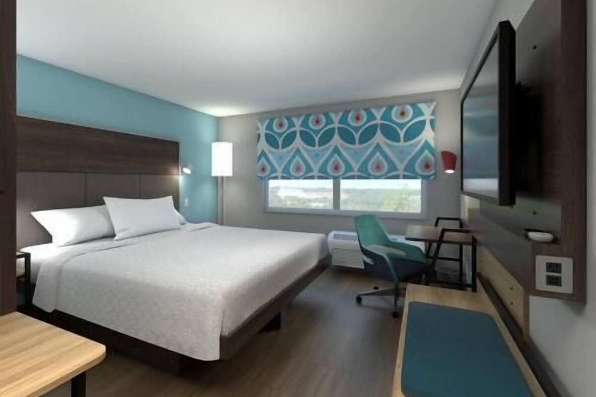 Une chambre d’hôtel équipée d’un lit, d’un bureau, d’une chaise, d’une télévision et d’une fenêtre avec des rideaux à motifs.