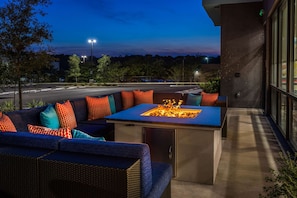 An outdoor seating area with a fire feature, a sofa with colorful cushions, and a view of a road and trees at dusk. - Tru By Hilton Pensacola Airport Medical Center (Pensacola)