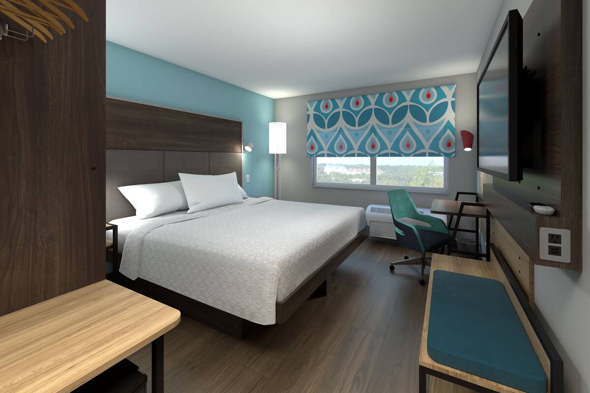 Une chambre d’hôtel moderne dotée d’un grand lit, de tables de chevet, d’un bureau, d’une chaise, d’une télévision et d’une fenêtre donnant sur la ville.