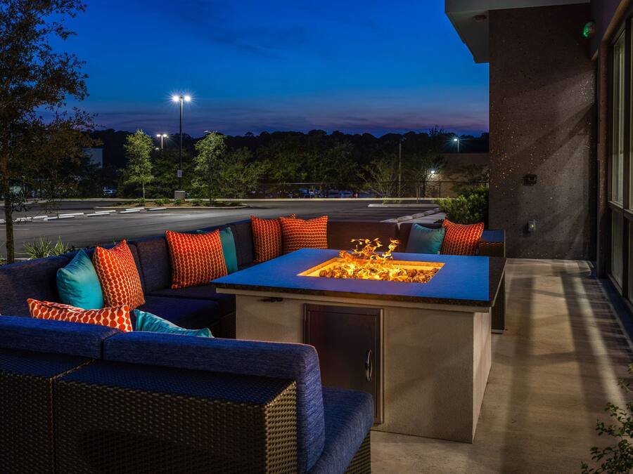 An outdoor seating area with a fire feature, a sofa with colorful cushions, and a view of the street at dusk.