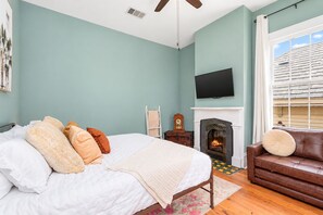 Une chambre à coucher avec un lit, une cheminée, un téléviseur et une fenêtre avec des stores.