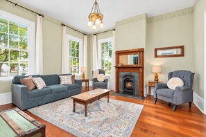 Een woonkamer met een open haard, een bank, een stoel, een salontafel en een kamerkleed met dessin.