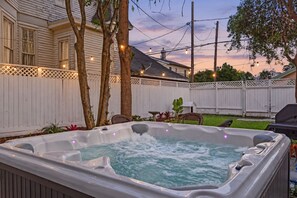 Een hottub in een achtertuin met een houten omheining, bomen en lichtjes.