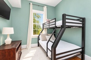 Een slaapkamer met stapelbed, een raam, een bureau met lamp en een aan de muur bevestigde televisie.