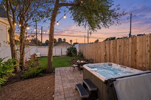 Un jardin avec un jacuzzi, des meubles de patio et des guirlandes lumineuses.