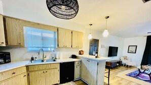 Una cocina moderna con armarios de madera, lavavajillas integrado y una isla grande. Hay un área de comedor con un sofá y una mesa de centro.