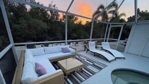 Un espacio de estar al aire libre cubierto con piscina, muebles de mimbre y vistas a los árboles circundantes.